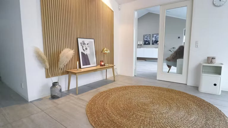 Minimale Scandinavische woonruimte met een rond jute vloerkleed, een houten bank met pampagras, ingelijste kunst en een Akupanel akoestische houten accentmuur.