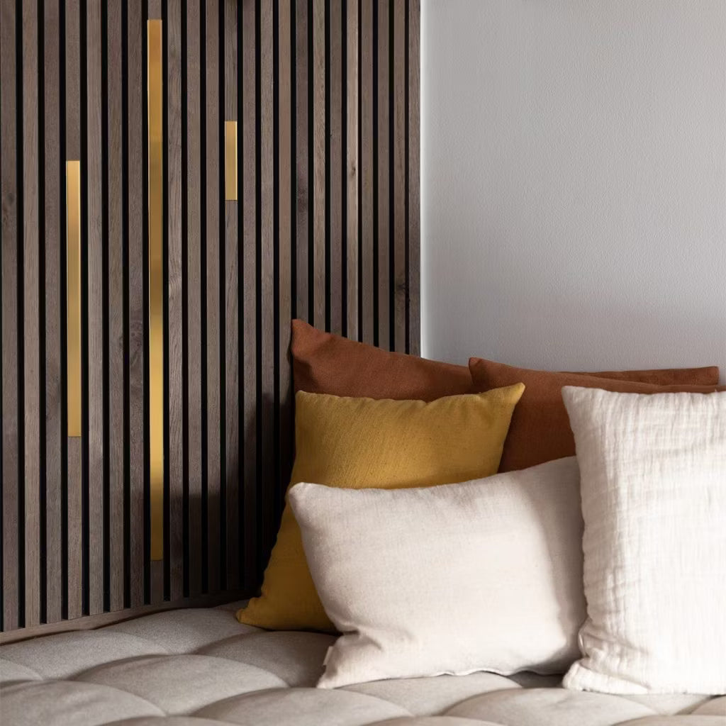 Crème, gele en bruine kussens op een beige getufte bank naast een modern akoestisch lamellenpaneel met gouden accenten voor een gezellige, eigentijdse omgeving.