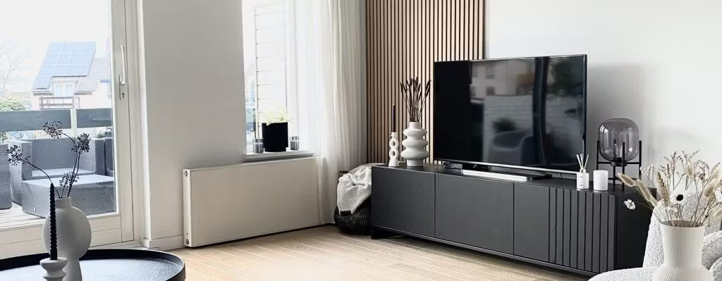 Moderne woonkamer met een zwart tv-meubel, flatscreentelevisie, decoratieve vazen en grote ramen met natuurlijk licht die uitkijken op de patio; Akupanel op één muur.