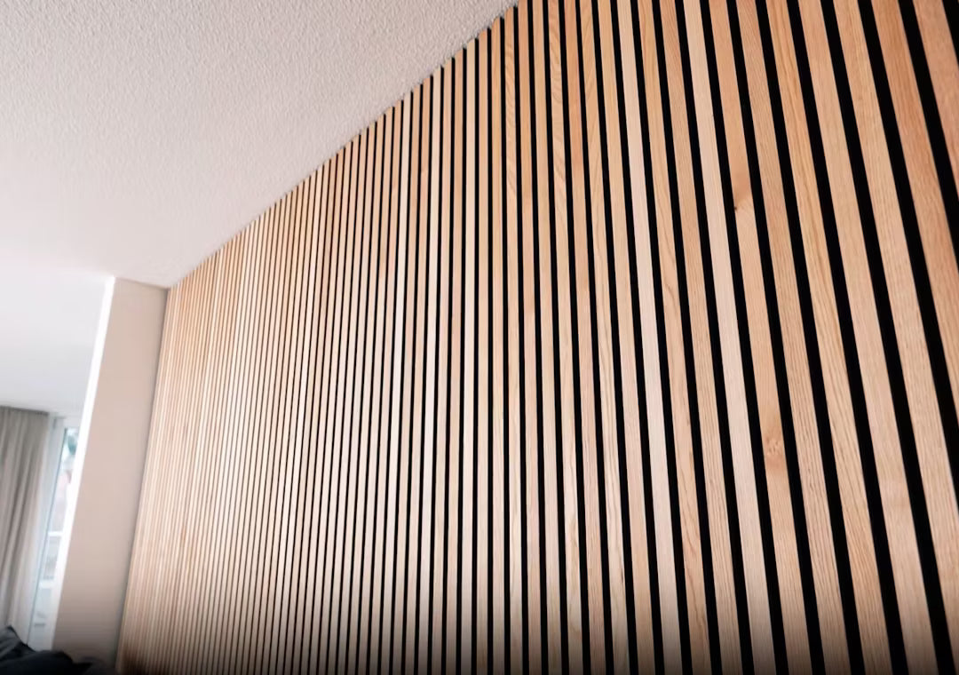 Close-up van Akupanel akoestisch houten paneel met verticale houten latten in een gestreept patroon, geïnstalleerd op een binnenmuur onder een wit plafond.
