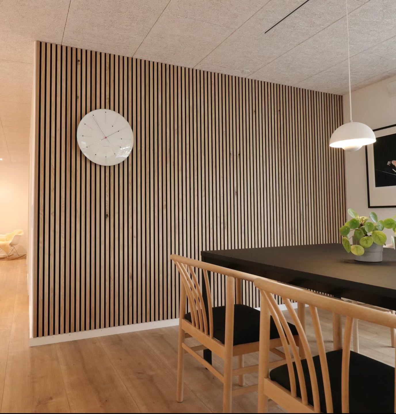 Moderne eetkamer met een Scandinavische Akupanel akoestische houten latten accentmuur, zwarte tafel, houten stoelen met zwarte zittingen en een potplanten middenstuk.
