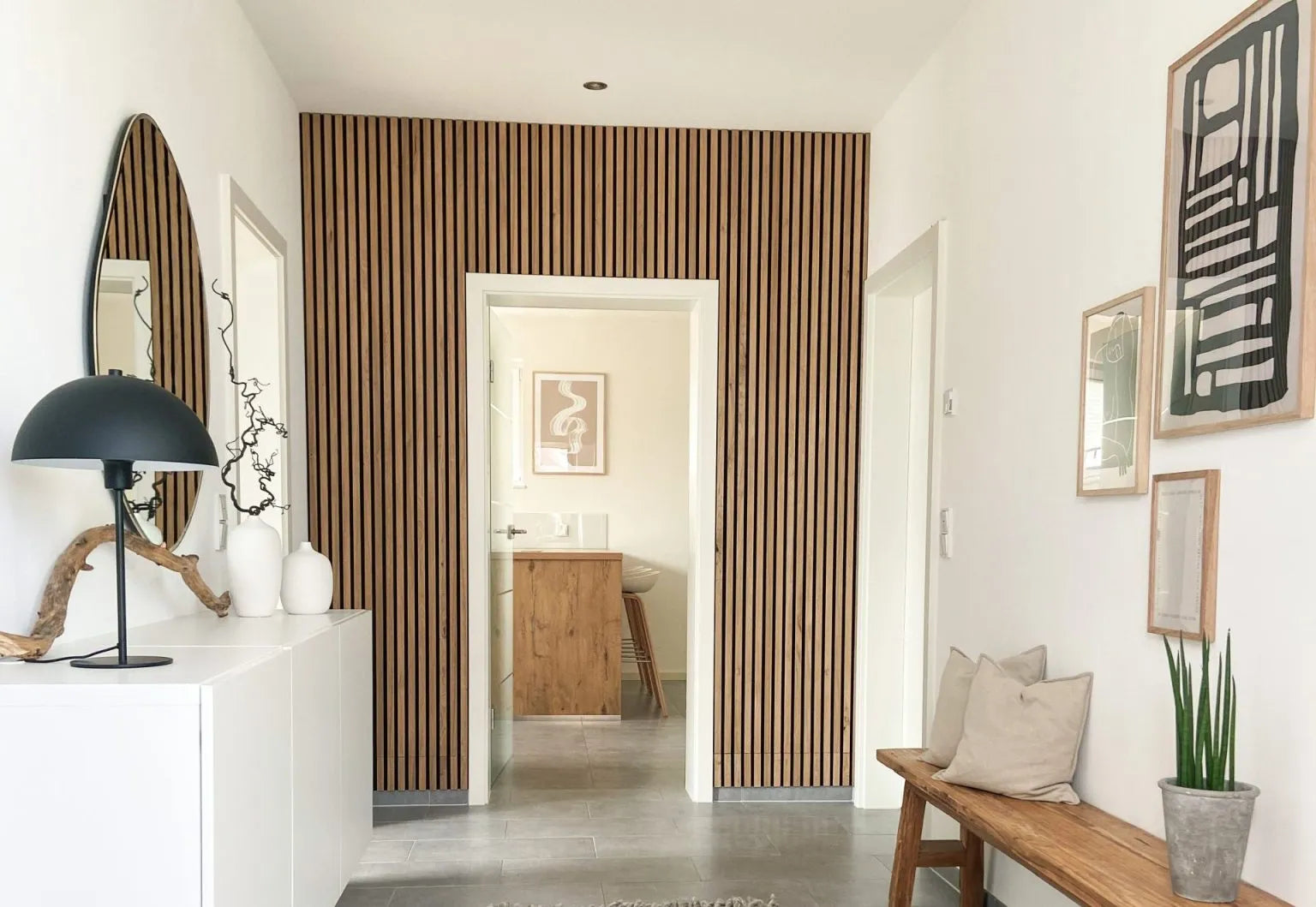 Een moderne hal met een akoestische accentmuur van Scandinavisch Akupanel hout, witte muren, een bank met kussens en een minimalistische inrichting.