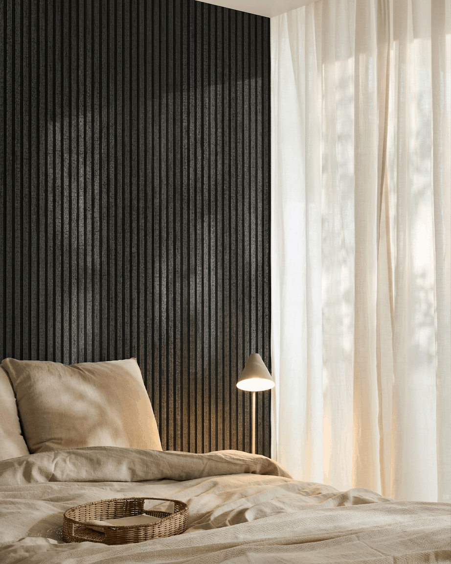 Sfeervolle slaapkamer met beige beddengoed, een rotan dienblad, witte lamp, transparante gordijnen en een WoodUpp Akupanel charcoal akoestisch houten paneel aan de muur.