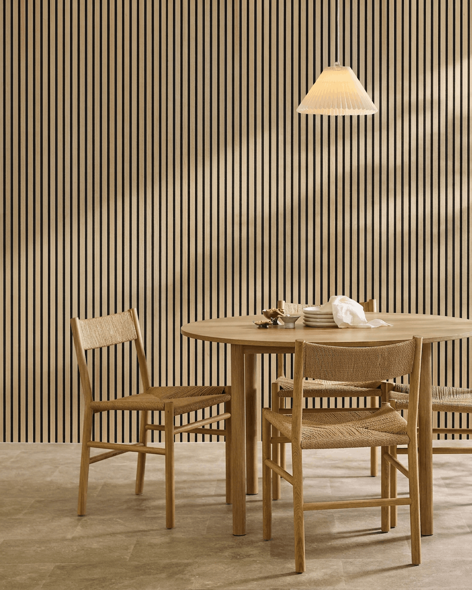 Minimalistische eethoek met een ronde tafel, geweven stoelen, hanglamp en een WoodUpp Akupanel Classic Oak Akoestisch paneel gemonteerd aan de muur.