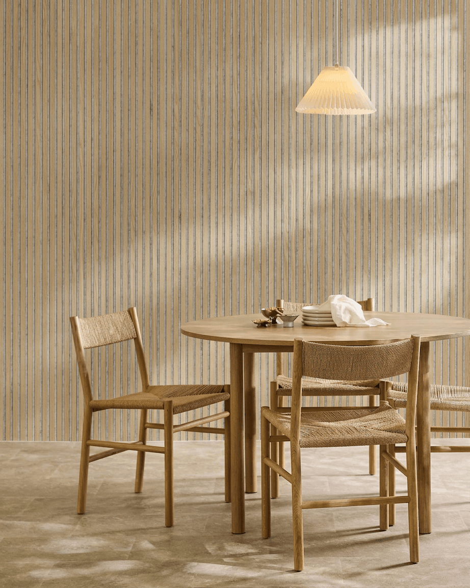 Minimalistische eethoek met een ronde houten tafel, geweven stoelen, een hanglamp en een WoodUpp Akupanel akoestisch houten paneel in Classic Oak met grey vilt.