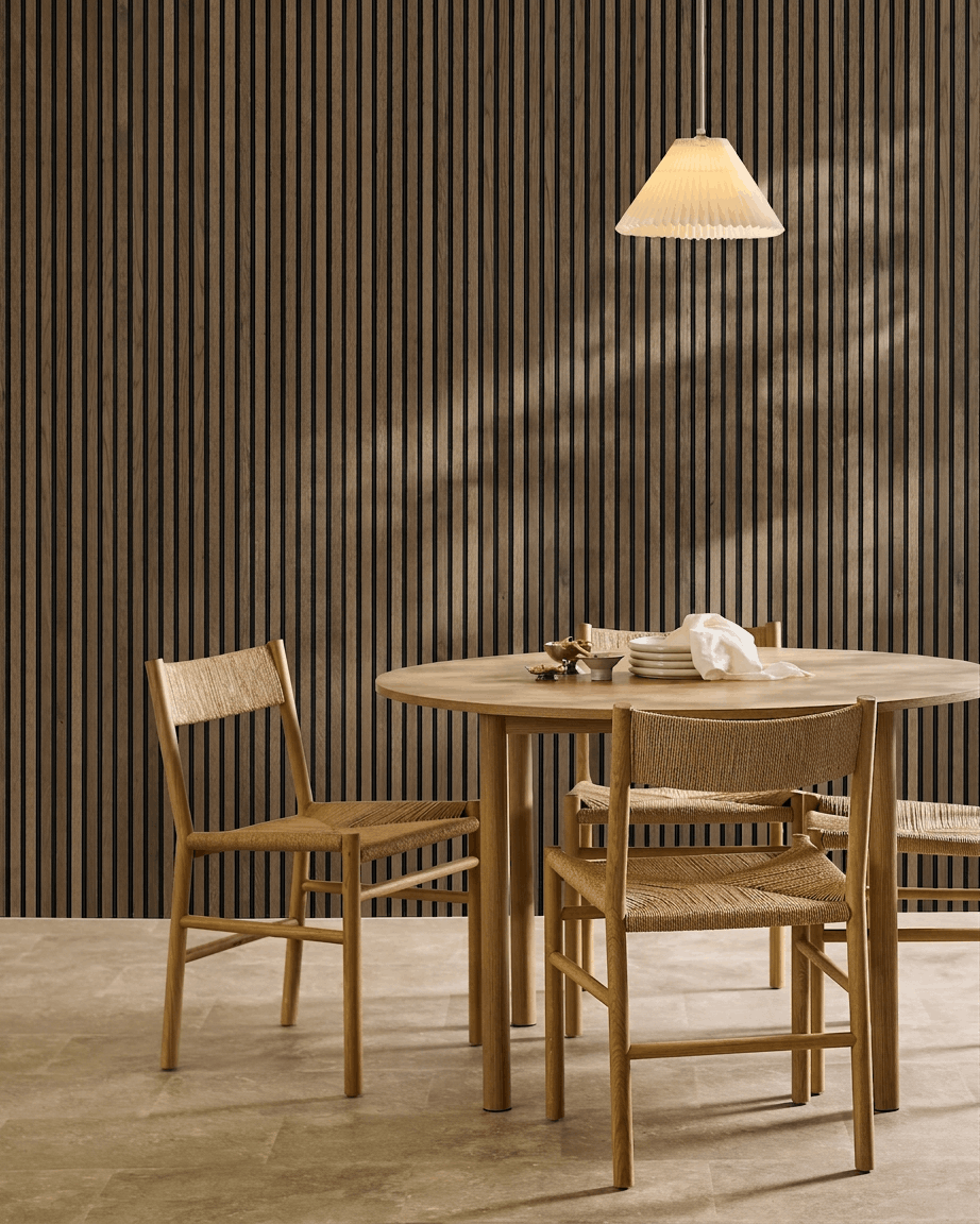 Minimalistische eethoek met ronde tafel, gevlochten stoelen en hanglamp, met een WoodUpp Akupanel Rustic Grey Oak akoestisch lattenwandpaneel.