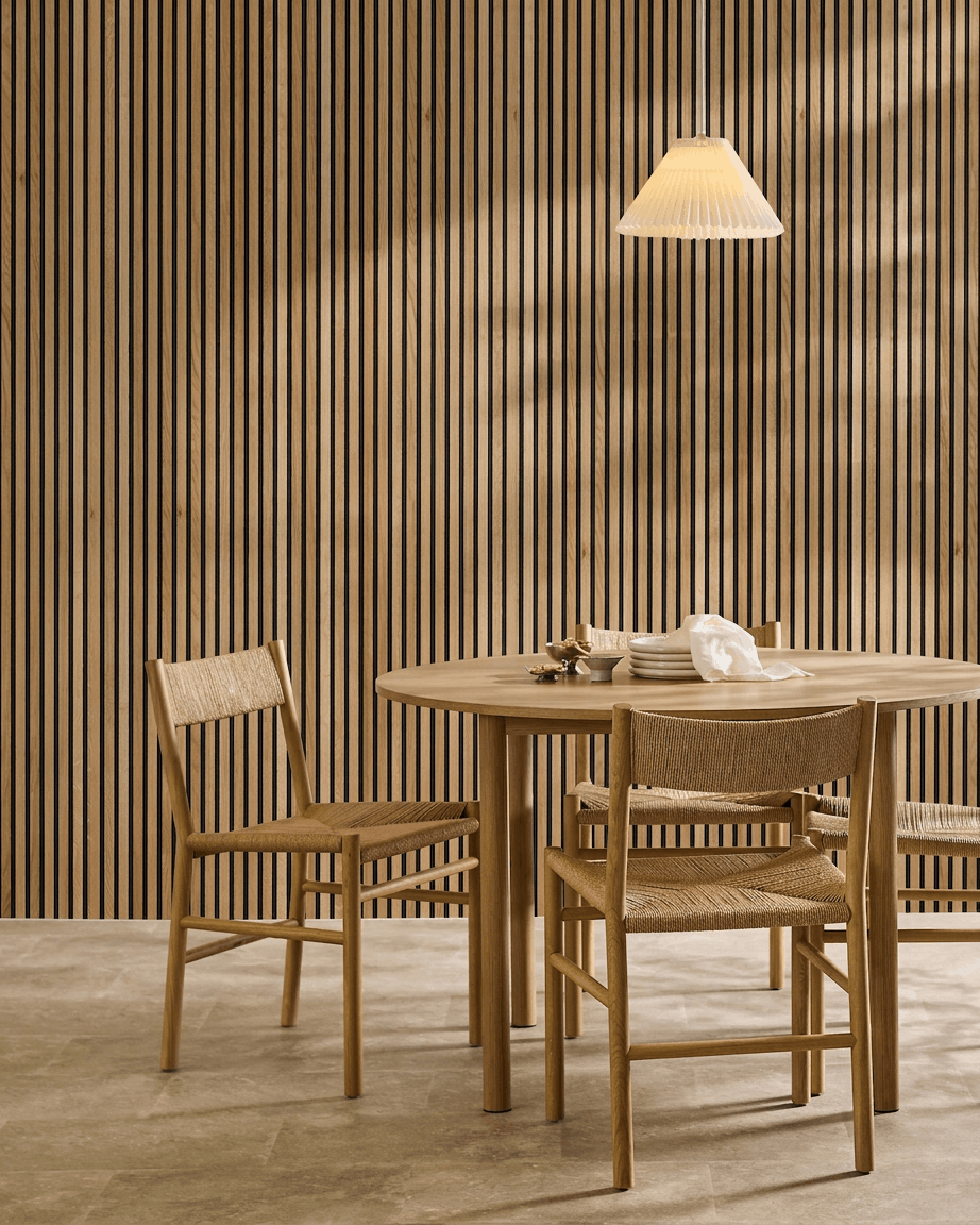 Minimalistische eethoek met een ronde tafel, geweven stoelen en een WoodUpp Akupanel akoestisch lattenwandpaneel in Rustic Natural Oak als Nordisch wandaccent.