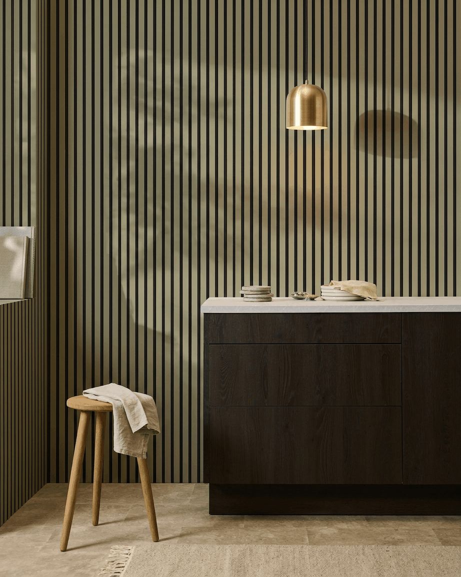 Moderne keuken met donkere houten kasten, marmeren werkblad, brass hanglamp, en een WoodUpp Akupanel Colored akoestisch lattenwandpaneel voor geluidsabsorptie.