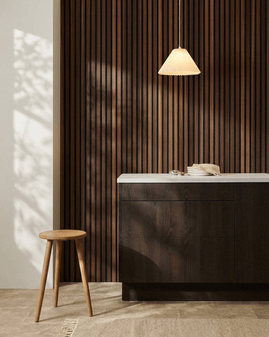 Minimalistisch interieur met een houten kruk, donkerhouten kast, hanglamp en een WoodUpp Akupanel akoestisch houten lattenwandpaneel in Natural Wood/Smoked Larch.
