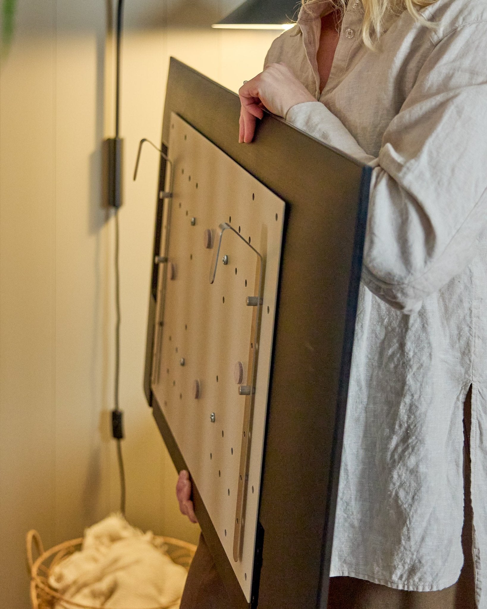Een persoon in een licht shirt houdt de WoodUpp Nell BM1 TV-Mount in beige, 64x44 cm—compatibel met Nordic akoestische houten panelen, voor installaties zonder muur.