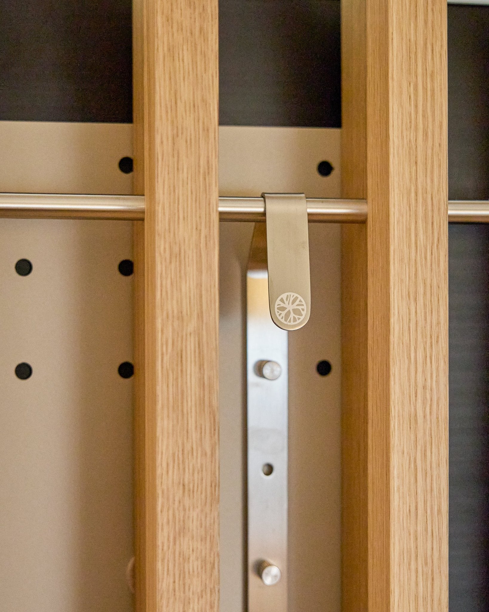 Een metalen zonnestraalclip bevestigd aan een houten lat op de WoodUpp Nell | TV-Mount BM1, Beige, 64x44 cm Akoestisch paneel kast met hoogteverstelling.