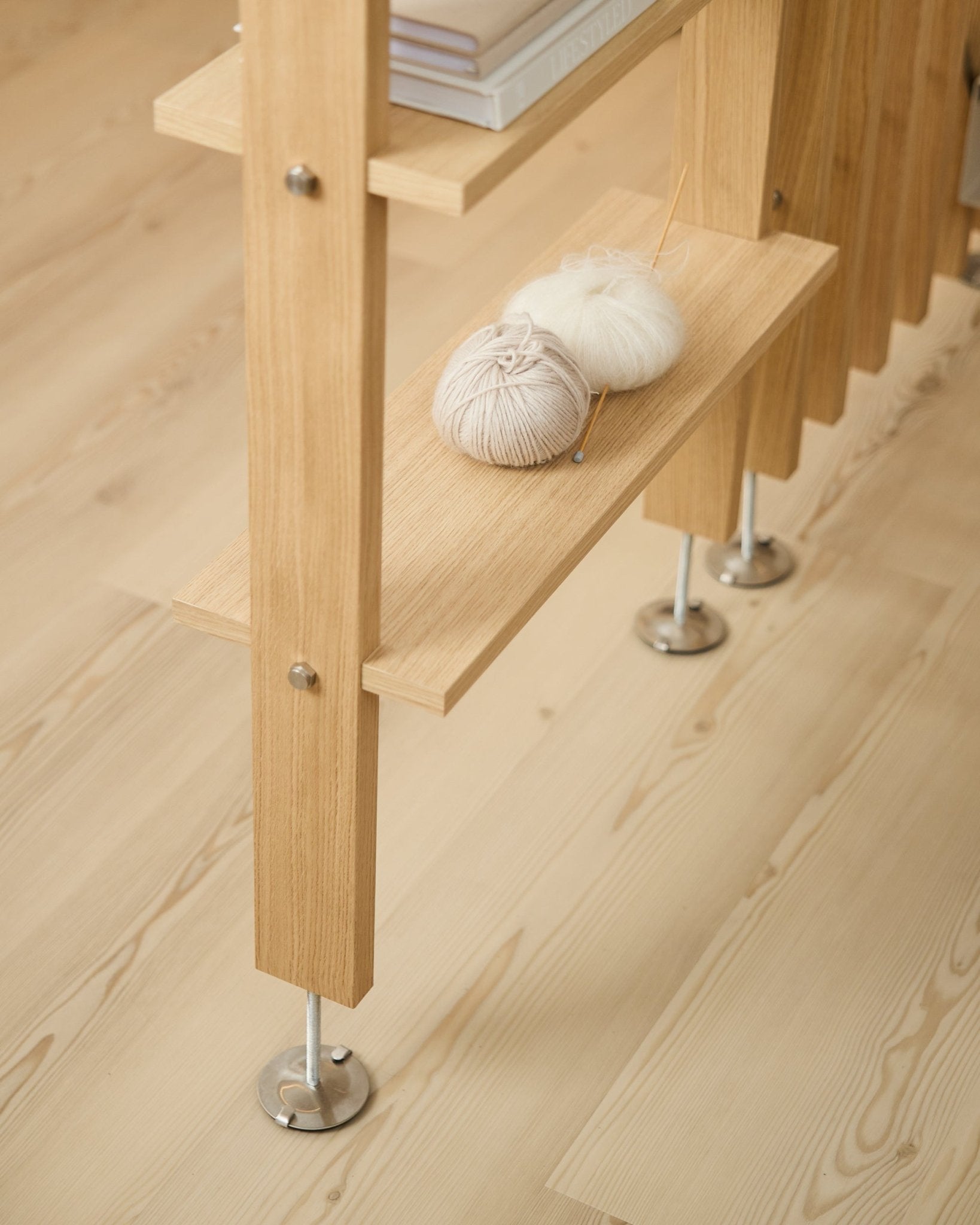 De Lova | Houten plank / BM2 van WoodUpp in eikenfineer (65,8x20 cm), met garen en breinaalden op de onderste plank, op een licht houten vloer met metalen poten.